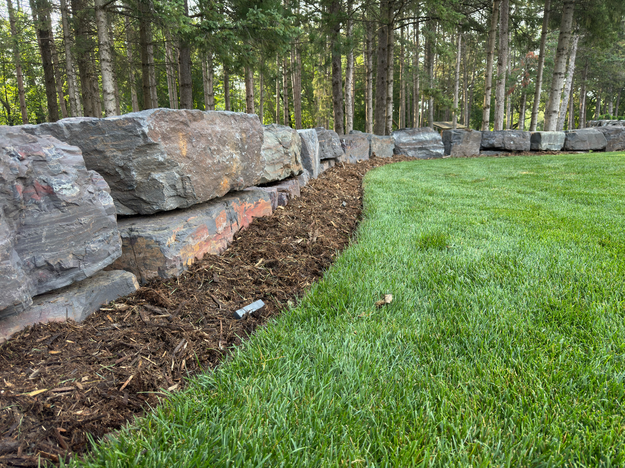 Natural stone boulder wall beside newly installed sod and mulch.