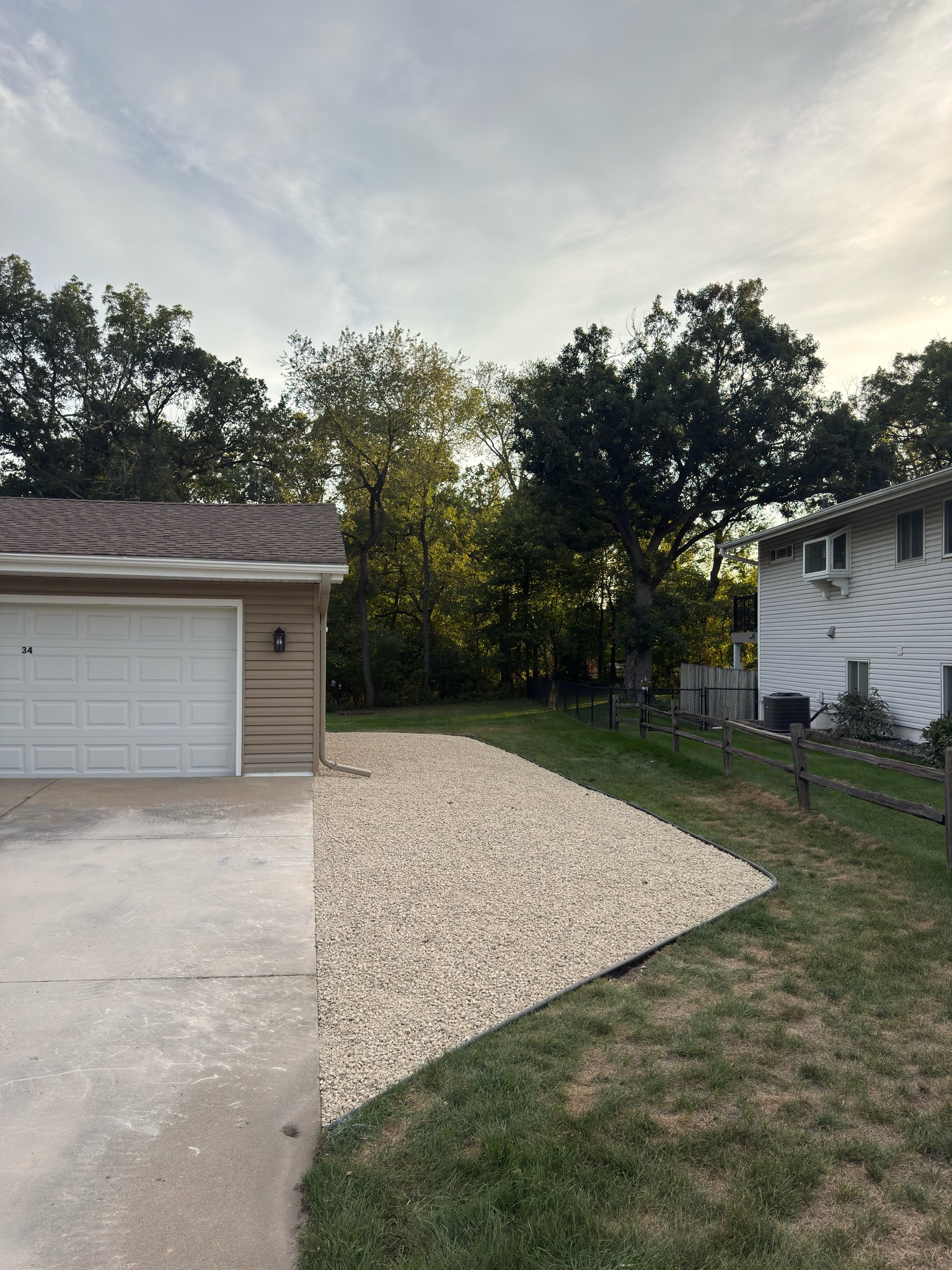 After: refreshed gravel parking area with clean curved edging beside the same garage and driveway.