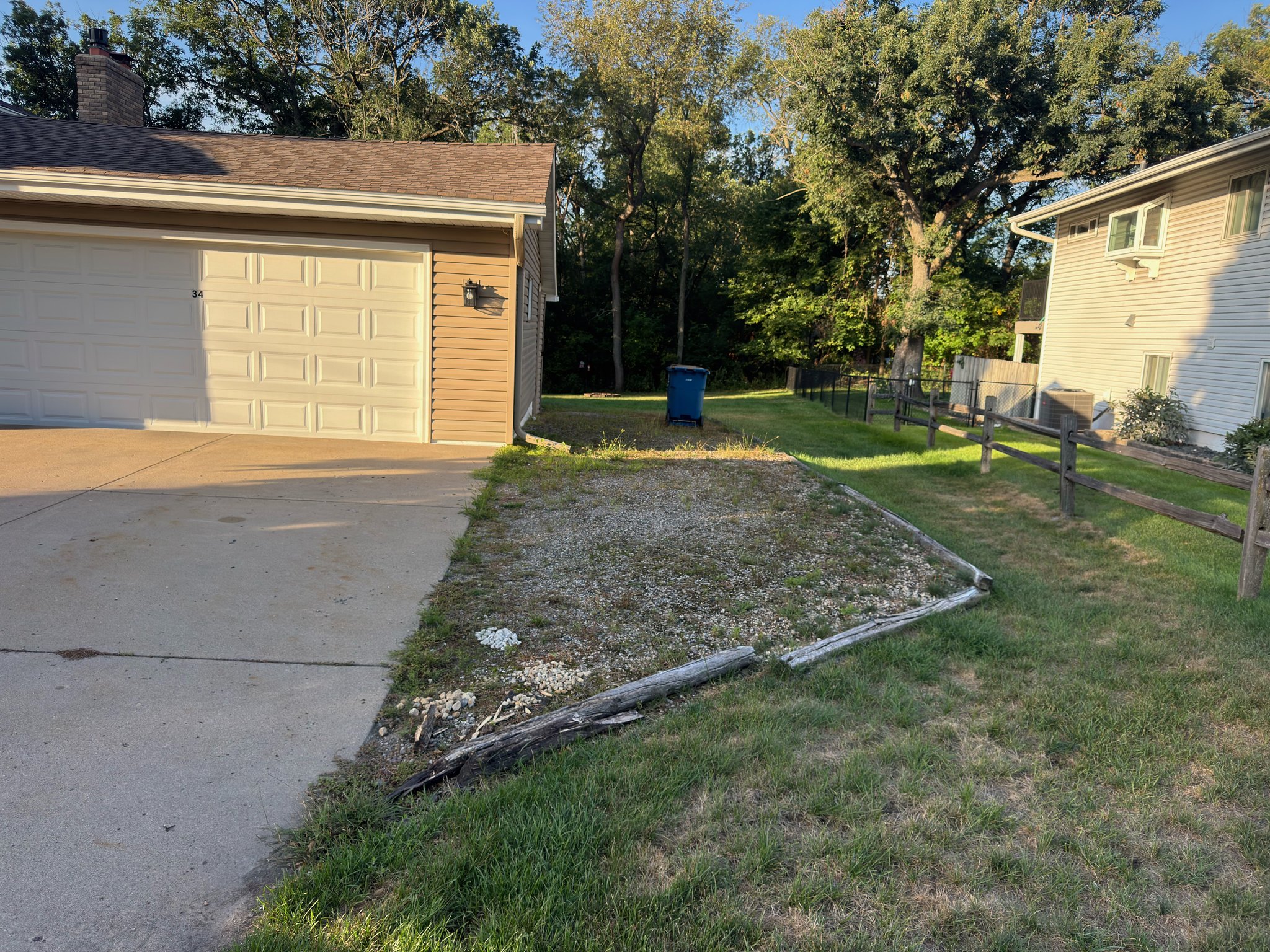 Before: weedy gravel area with worn timber edging beside the garage and concrete driveway.