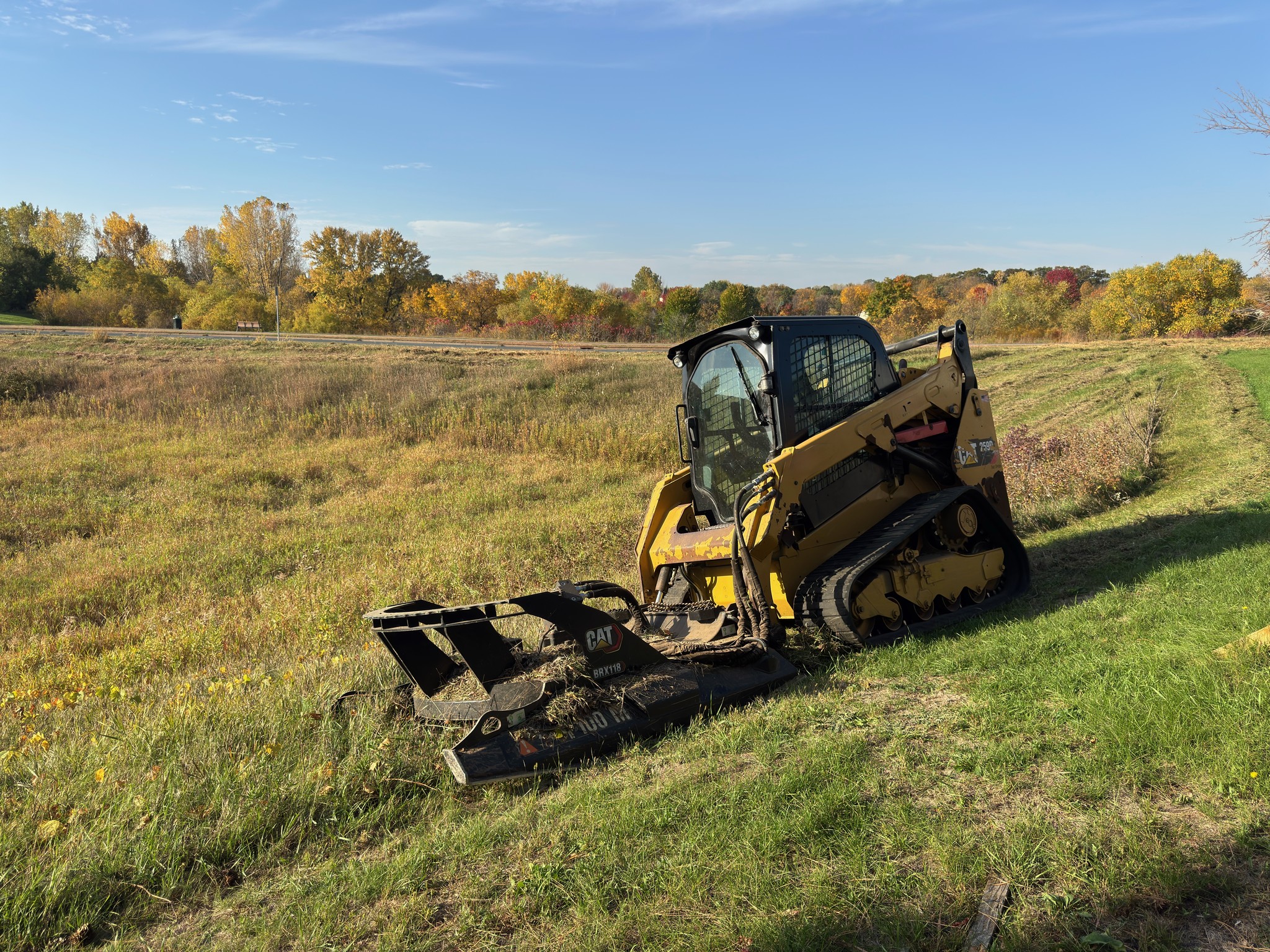 SPS CAT tracked skid loader with a brush mower parked on the right side of an open field.