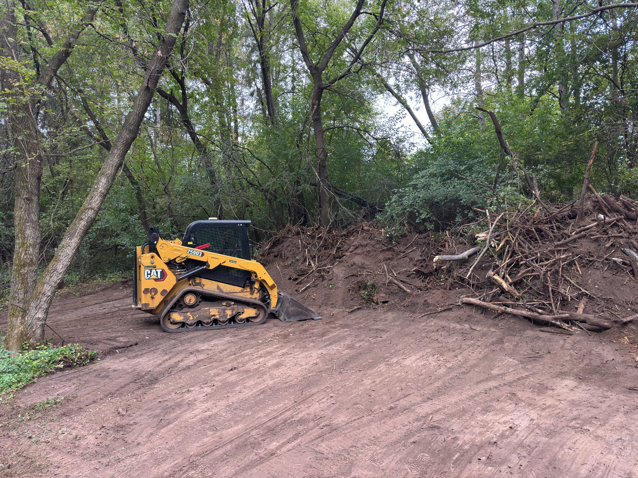 SPS CAT tracked loader beside cleared ground and brush piles on a wooded property.